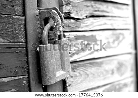 A black and white photograph of an old rusted lock sees on a wooden barn door. Prohibition concept. Protection against thieves and robbers, there is no way further. Fears hide under lock and key.