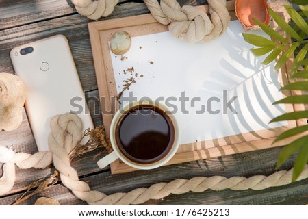 Mock up with empty wooden frame, rope, phone and cup of coffee, outdoor summer photo, marine style, palm shadows