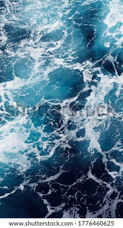Vertical photo. Background of blue ocean water. Aerial view of foam stains on the water.