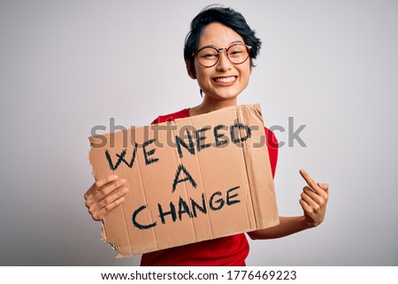 Beautiful asian girl protesting holding banner with change message over white background very happy pointing with hand and finger