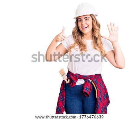 Young caucasian woman wearing security helmet showing and pointing up with fingers number six while smiling confident and happy. 