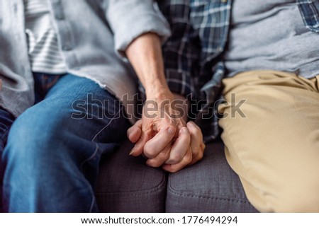 cropped view of senior couple sitting on sofa and holding hands 