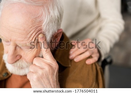 cropped view of woman touching shoulder of husband, sick on dementia, sitting with closed eyes and touching head Royalty-Free Stock Photo #1776504011