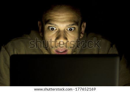 A man with a shocked look on his face at night on his laptop. Royalty-Free Stock Photo #177652169