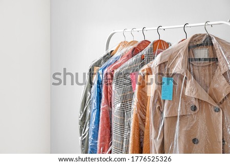 Rack with clothes after dry-cleaning on light background Royalty-Free Stock Photo #1776525326
