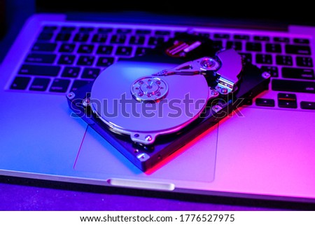 The disassembled hard drive lies on the laptop keyboard. Neon blue-red light.