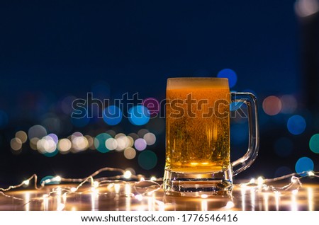 A glass of beer on wooden table with colorful city bokeh light background.
