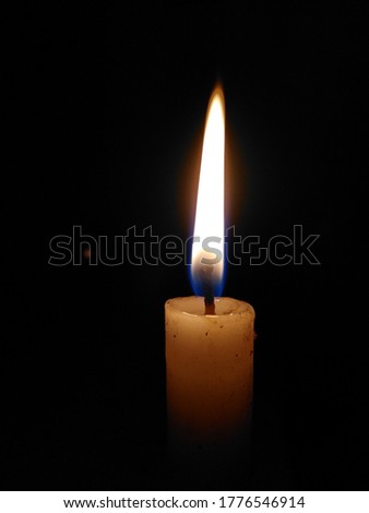 Picture of burning candle in night with yellow flame and black background.