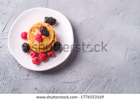 Cottage cheese pancakes, curd fritters dessert with raspberry and blackberry berries in plate on stone concrete background, top view copy space