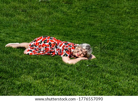 beautiful girl with a dress with red poppies on a green lawn in a park