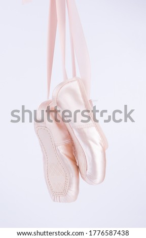 New pink ballet shoes hanging on white background.