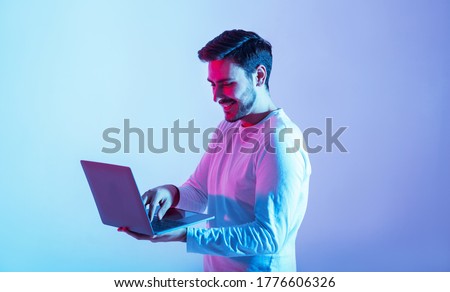 Work and play online. Happy guy holding laptop and typing in neon light, copy space