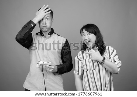 Young handsome businessman and mature Asian businesswoman against gray background