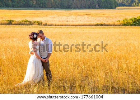 Wedding couple shares a romantic moment in a field or meadow at sunset on their wedding day.