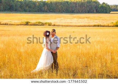 Wedding couple shares a romantic moment in a field or meadow at sunset on their wedding day.