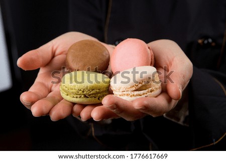 colorful macarons held by two hands showing them, isolated on a black background