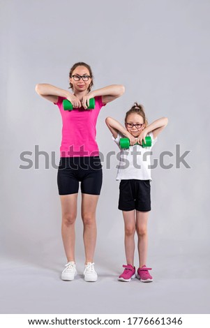 Stylish mom and daughter stand on a gray background in sportswear and with dumbbells. Active lifestyle, fitness. Sport family.