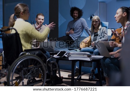 Handicapped young woman with colleagues working in office. She is smiling and passionate about the workflow. Performing in co-working space. Office people working together. Royalty-Free Stock Photo #1776687221