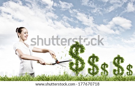 Young attractive businesswoman cutting plant in shape of dollar