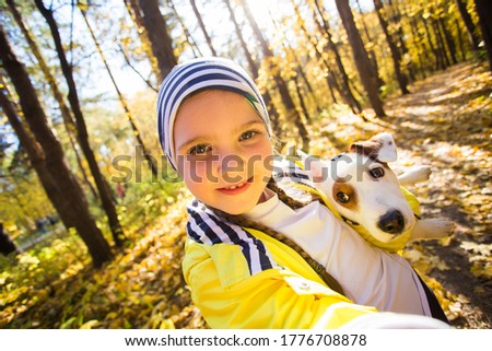 Little girl taking selfie with her dog at autumn park. Child posing with jack russell terrier for a picture on the mobile phone outdoors. Pet and children concept.