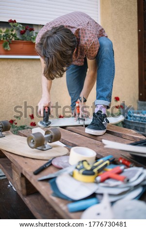 Carpenter polishing wooden board with sander. Repairman processing skateboard deck with sanding machine outdoor.