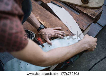 Top view of male hands polishing wooden board. Man's hands using sander and polishing wooden skateboard deck outdoor.