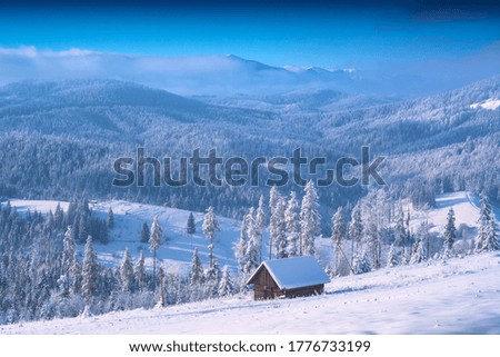 Lonely wooden house on a hill covered with fresh snow in a mountain valley. Majestic frozen winter picture.