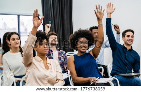 Group of young people sitting on conference together while raising their hands to ask a question. Business team meeting seminar training concept. Royalty-Free Stock Photo #1776738059