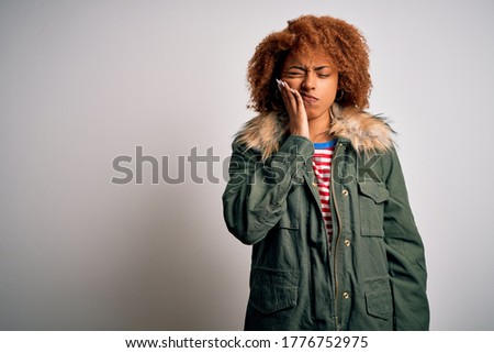 Young beautiful African American woman with curly hair wearing green casual winter coat touching mouth with hand with painful expression because of toothache or dental illness on teeth. Dentist