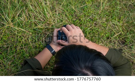 Close-up image of photographer laying on the grass during photo session. Photographed at different angle, outdoor.
