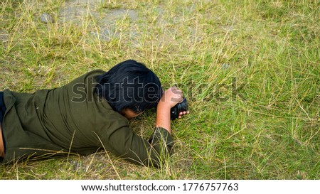 Close-up image of photographer laying on the grass during photo session. Photographed at different angle, outdoor.