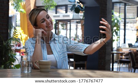 Happy young woman taking selfie in the cafe. Portrait of a happy woman taking a photo with modern smartphone. Casual cheerful woman taking selfie smiling.