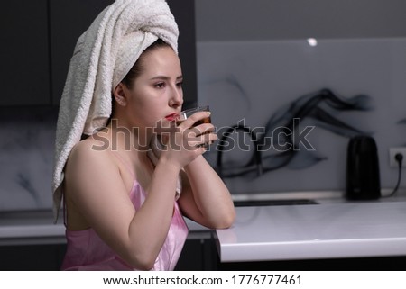 attractive brunette girl - in pink pajamas and with white towel on her head - with glass of whiskey, in kitchen. High quality photo