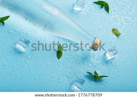 Cold Water Bottle, ice cubes, drops and mint leaves on a blue background.
