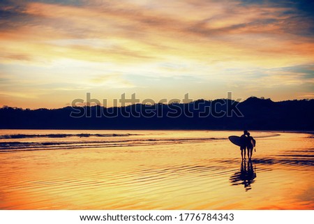 Low tide and wet sand reflecting the golden color of sunset on a beach with a surfer out of the water Royalty-Free Stock Photo #1776784343