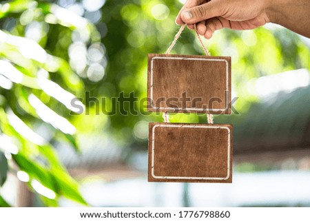 A hand holding blank wooden sign and a green bokeh background of the leaves