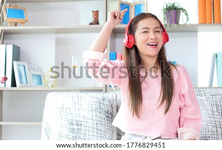Beautiful Asian woman relaxing and listening music with headphone in living room at home.