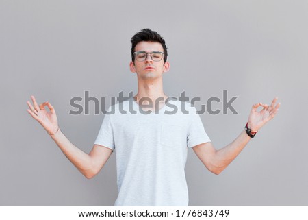 Concentrated relaxed man standing with closed eyes, having relaxation while meditating, trying to find balance and harmony. Yoga and meditation concept
