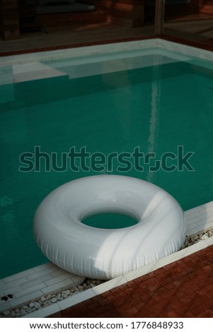 A white swimming ring is beside to a pool in evening time.