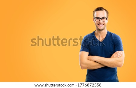 Portrait of happy man in glasses, casual smart clothing, with crossed arms. Orange color background, with copy space for some text. Caucasian male model in glasses at studio picture.