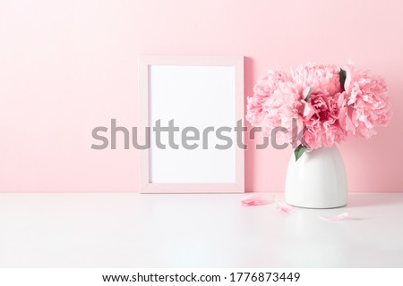 Home interior floral decor with pink peonies on shelf. Front view blank mock up of photo frame. Beautiful flowers pink peonies in vase on white background.