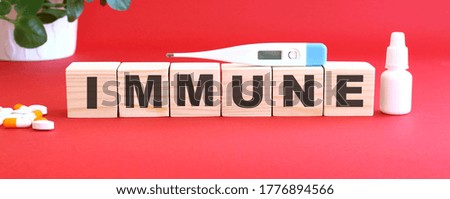 The words IMMUNE is made of wooden cubes on a red background with medical drugs. Medical concept.