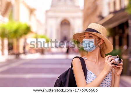 Portrait shot of beautiful blond woman wearing face mask for prevention while using vintage camera to taking photos in the city. 