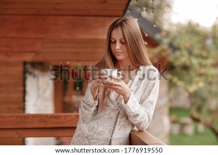 Young female standing after taking a shower in the morning on balcony of the hotel. holding a cup of coffee or tea in her hands. Looking outside nature forest and Mountain.