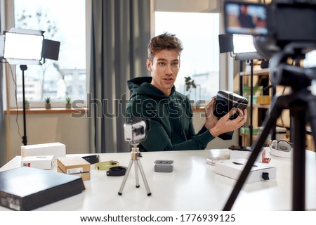 Young male technology blogger recording video blog or vlog review of new vr glasses, headset and other gadgets at home studio. Blogging, Work from Home concept. Selective focus. Horizontal shot Royalty-Free Stock Photo #1776939125