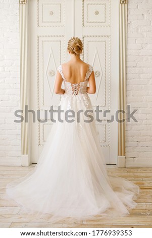 wedding day, the bride in a white long dress stands near a large wooden door, vertical picture, a blonde girl with a beautiful braided hairdo