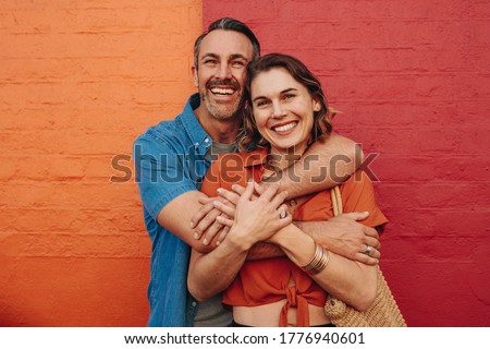 Portrait of affectionate mature couple embracing each other against red and orange background and smiling.