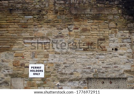 large old outdoor brown stone wall with a parking sign that reads permit holders only