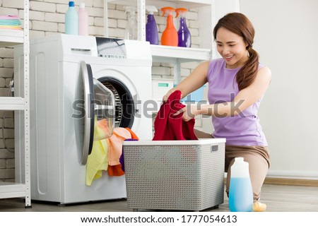 Asian housewife is separating clothes from the basket and put them into the washing machine for laundry. Young woman is happily doing housework.
