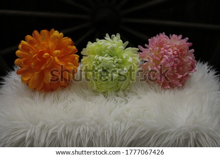 A horizontal photo of orange , green and pink flowers laying on a white rug.